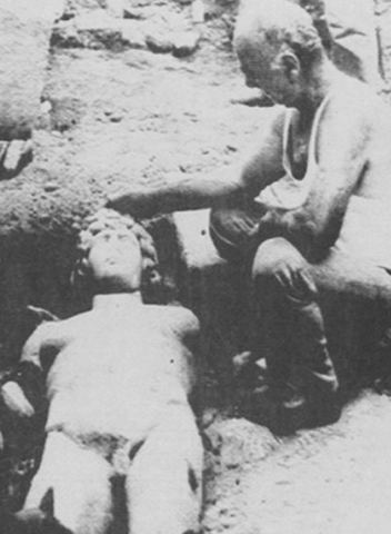 Black-and-white photograph of the marble statue of Antinoos lying in the earth at its find-spot near Myloi.