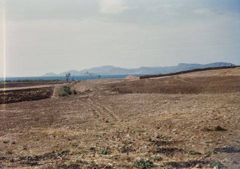 Distant view of the Lerna site across dry fields, with the bay beyond.