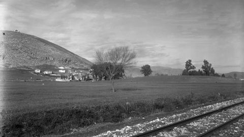 The prehistoric mound of Lerna from the south-east with metre-gauge rails in the foreground, Pontinos and the southern houses of Myloi, and eucalyptus trees.