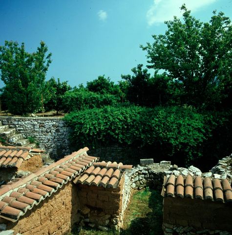 Lerna excavation: walls under small tiled roofs, a dry-stone boundary wall and an orchard.