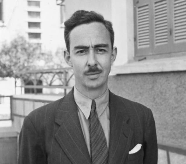Zwart-witportret van John L. Caskey in krijtstreeppak met das