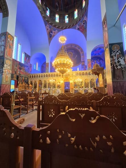Inside the church of the Holy Apostles: carved wooden pews, a golden chandelier under the painted dome and the gilded iconostasis