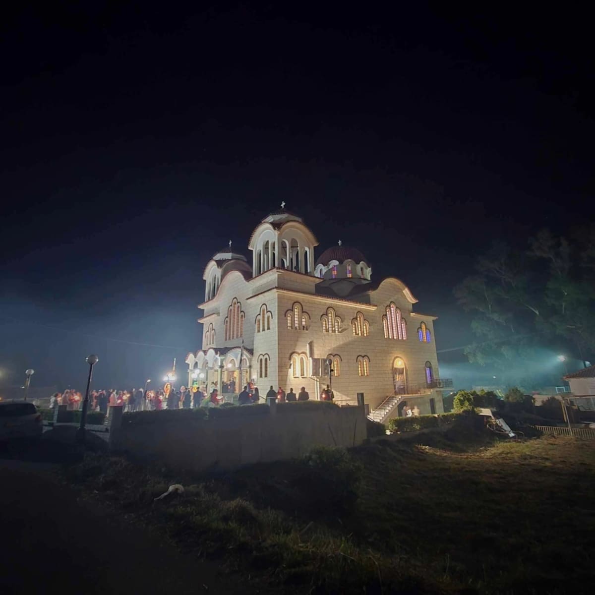 The Holy Apostles church lit up on Easter night, with people holding candles outside