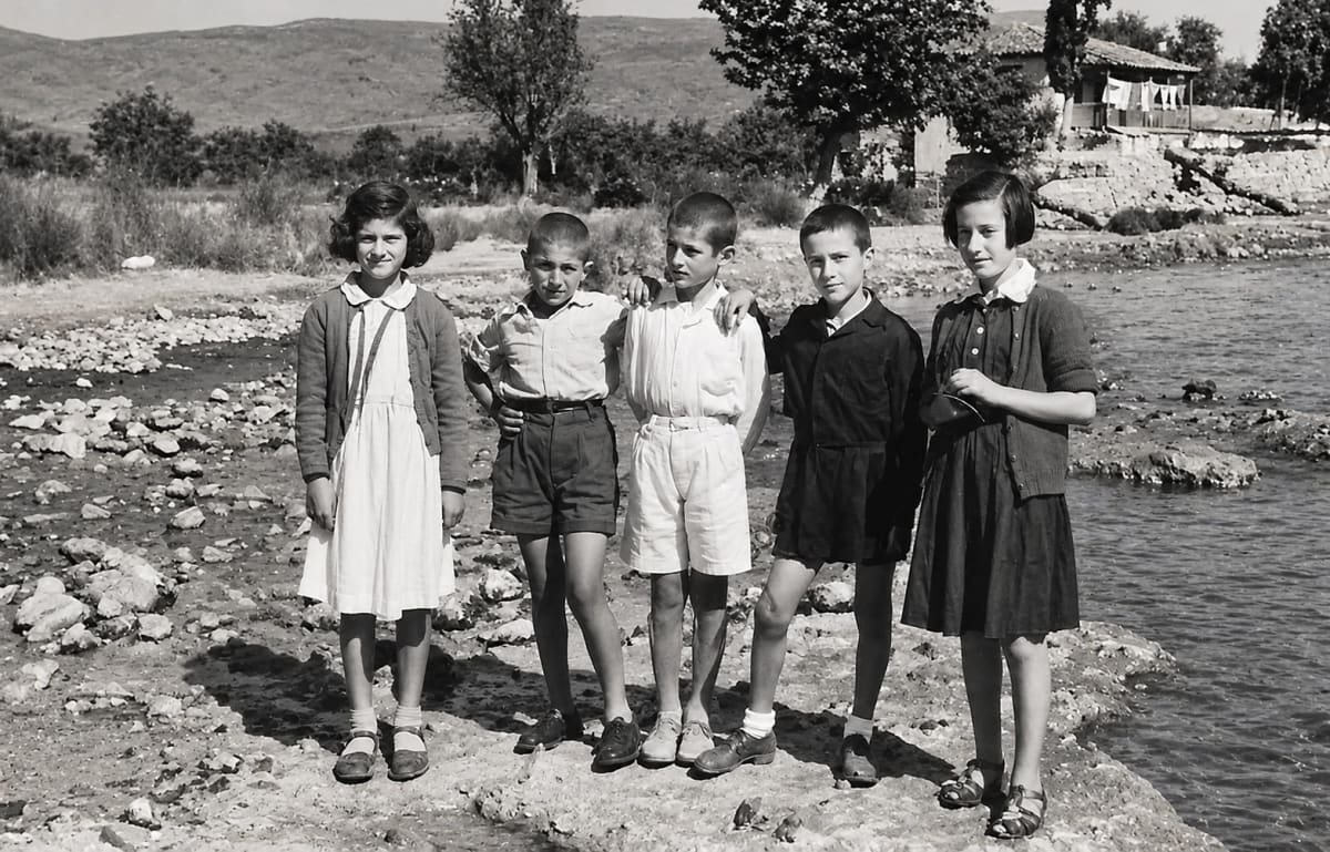 Five children standing side by side on the stony bank of the water (digitally restored)