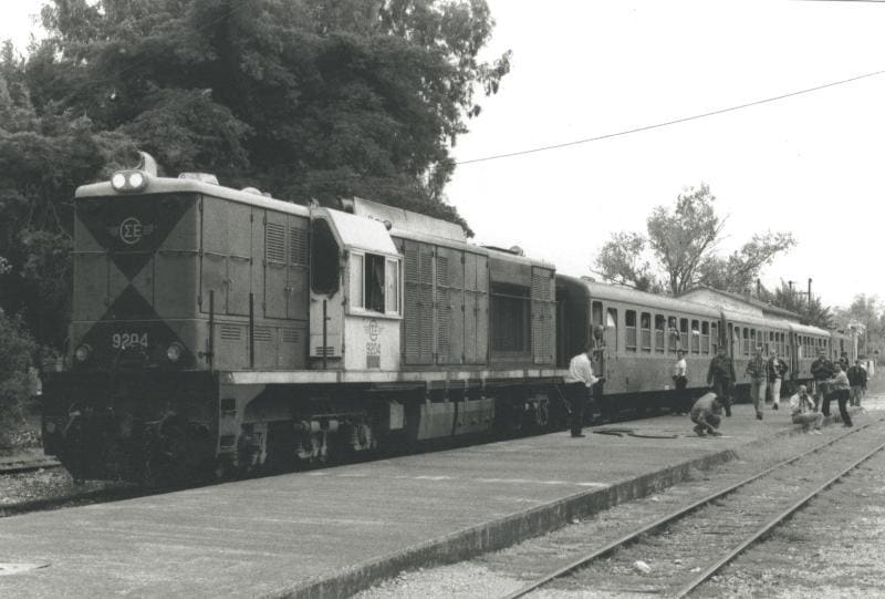 Czarno-białe zdjęcie lokomotywy spalinowej i pociągu pasażerskiego na stacji Myloi