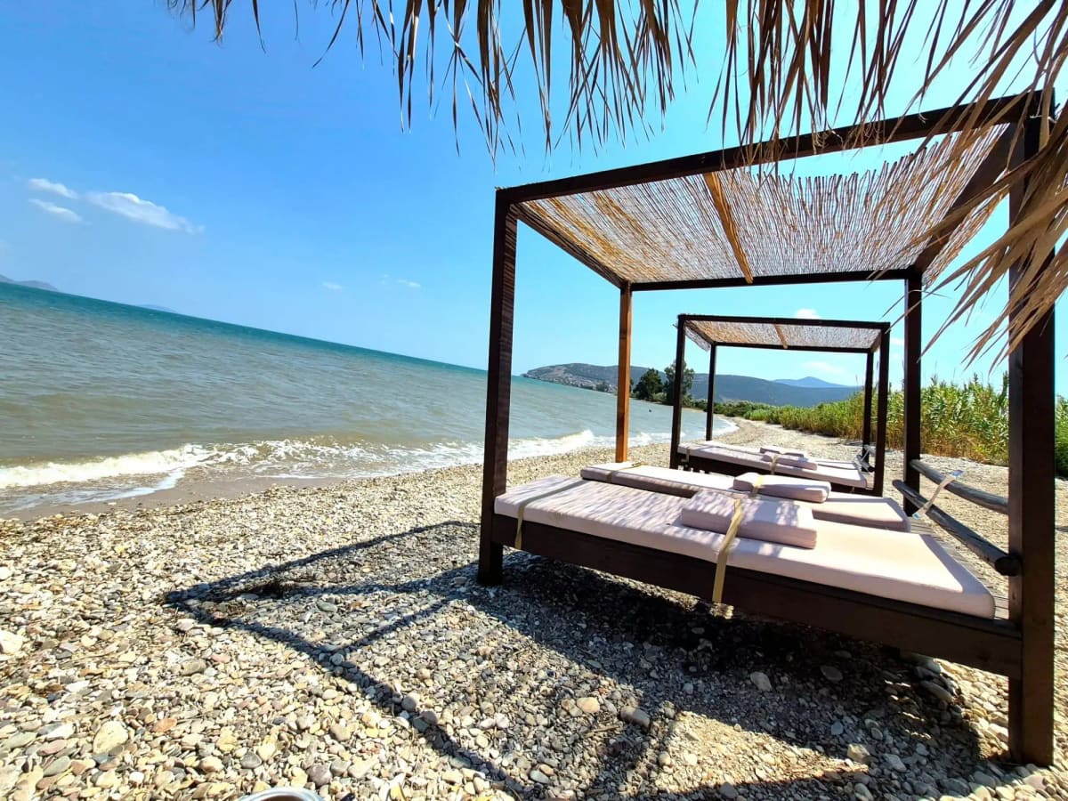 Shaded daybeds with cushions on the pebble beach at Aqua beach bar, the sea on the left
