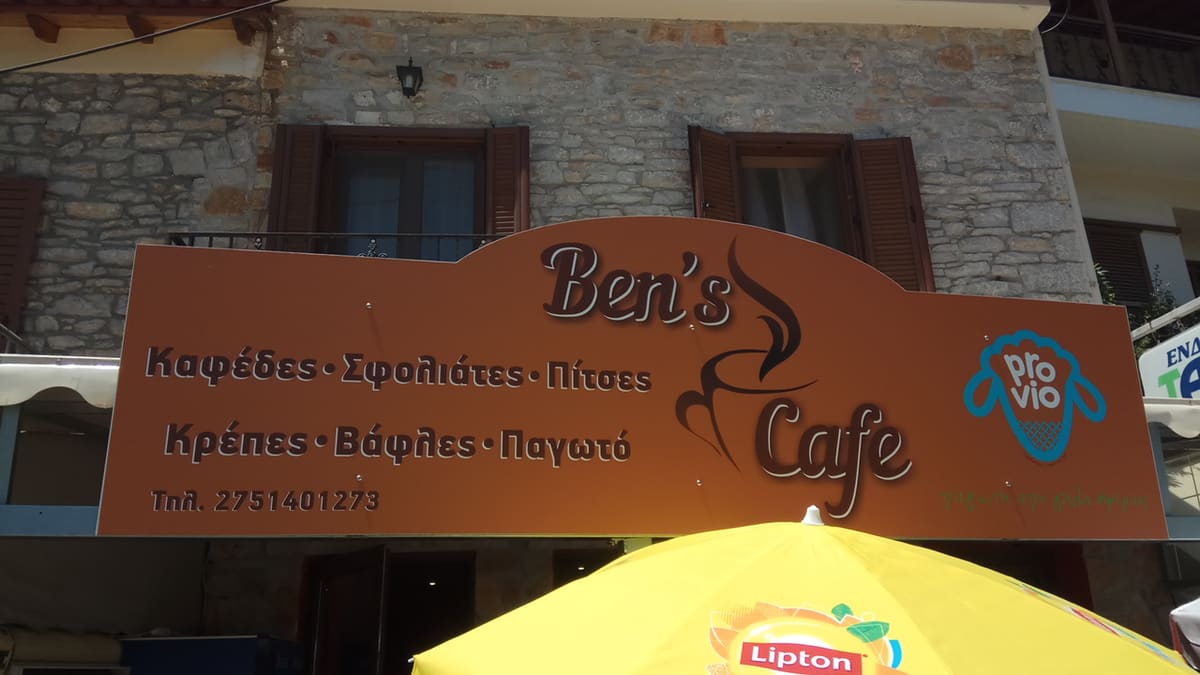 The orange sign of Ben's Cafe on a stone building, listing coffee, pies, pizza, crêpes, waffles and ice cream
