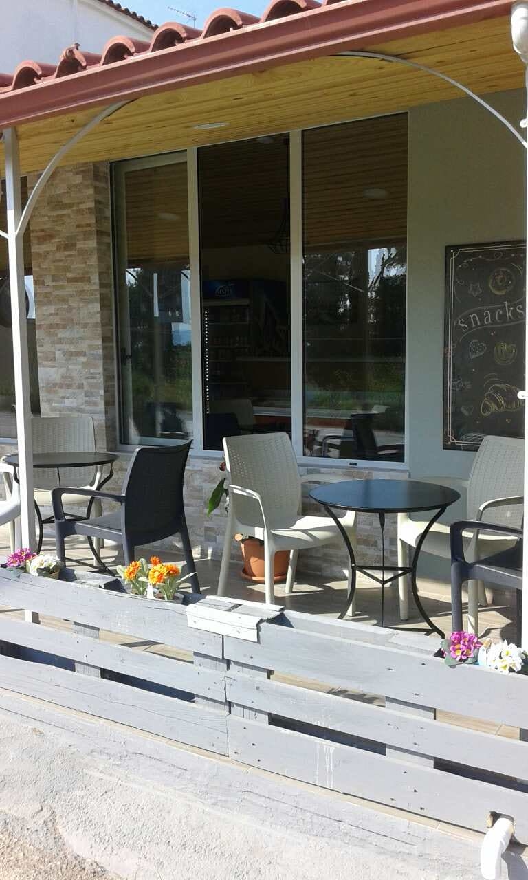The covered terrace of Coffee Way with grey chairs, round tables and flower boxes