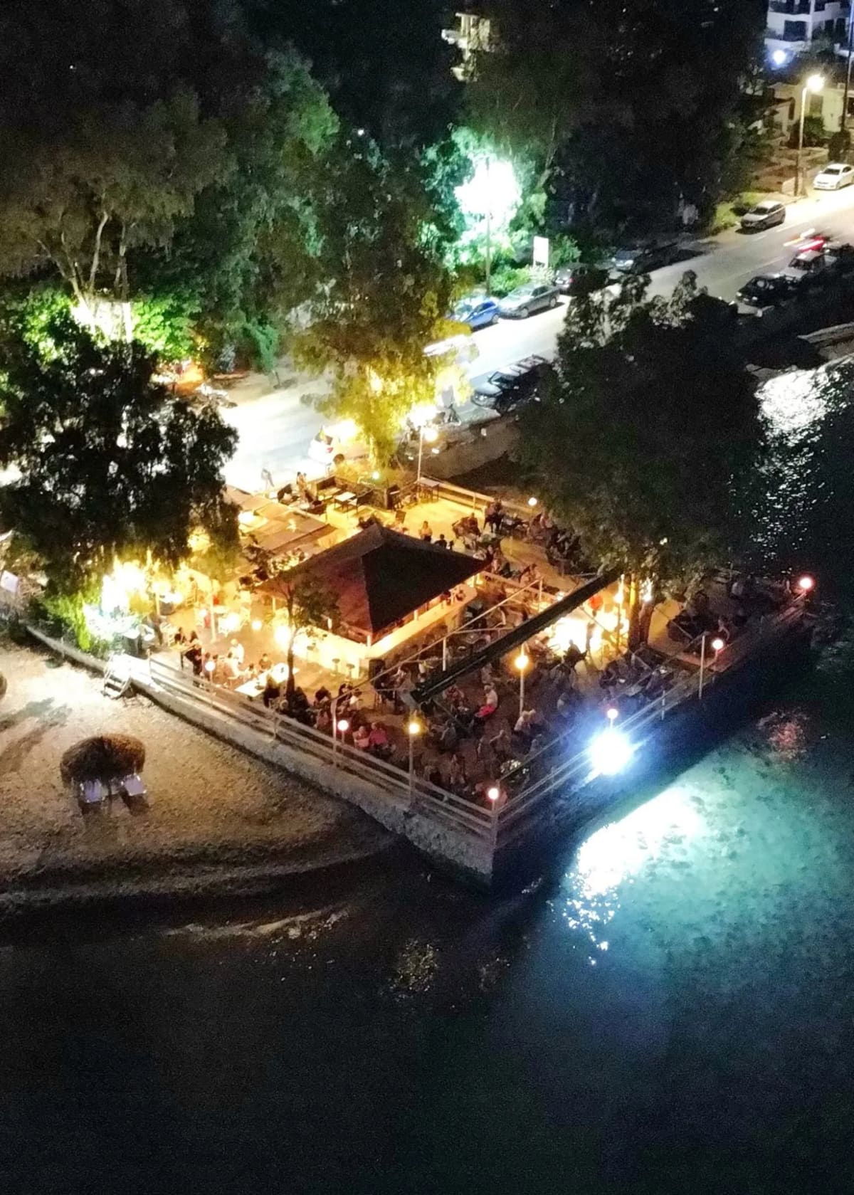 Café-bar Grammes 's avonds van bovenaf: een druk, verlicht terras aan het water naast het strand