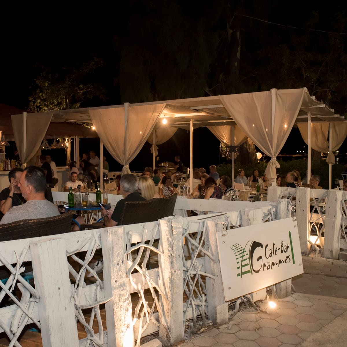 The Grammes cafe-bar terrace at night with white drapes and soft lights
