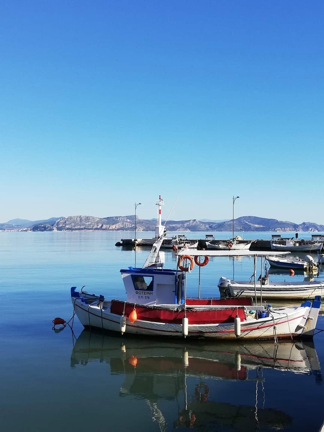 Małe łodzie rybackie odbite w spokojnej wodzie portu w Myloi pod czystym niebem