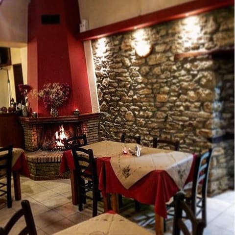 Stone-walled dining room with a fireplace and red tablecloths at To Mikraki