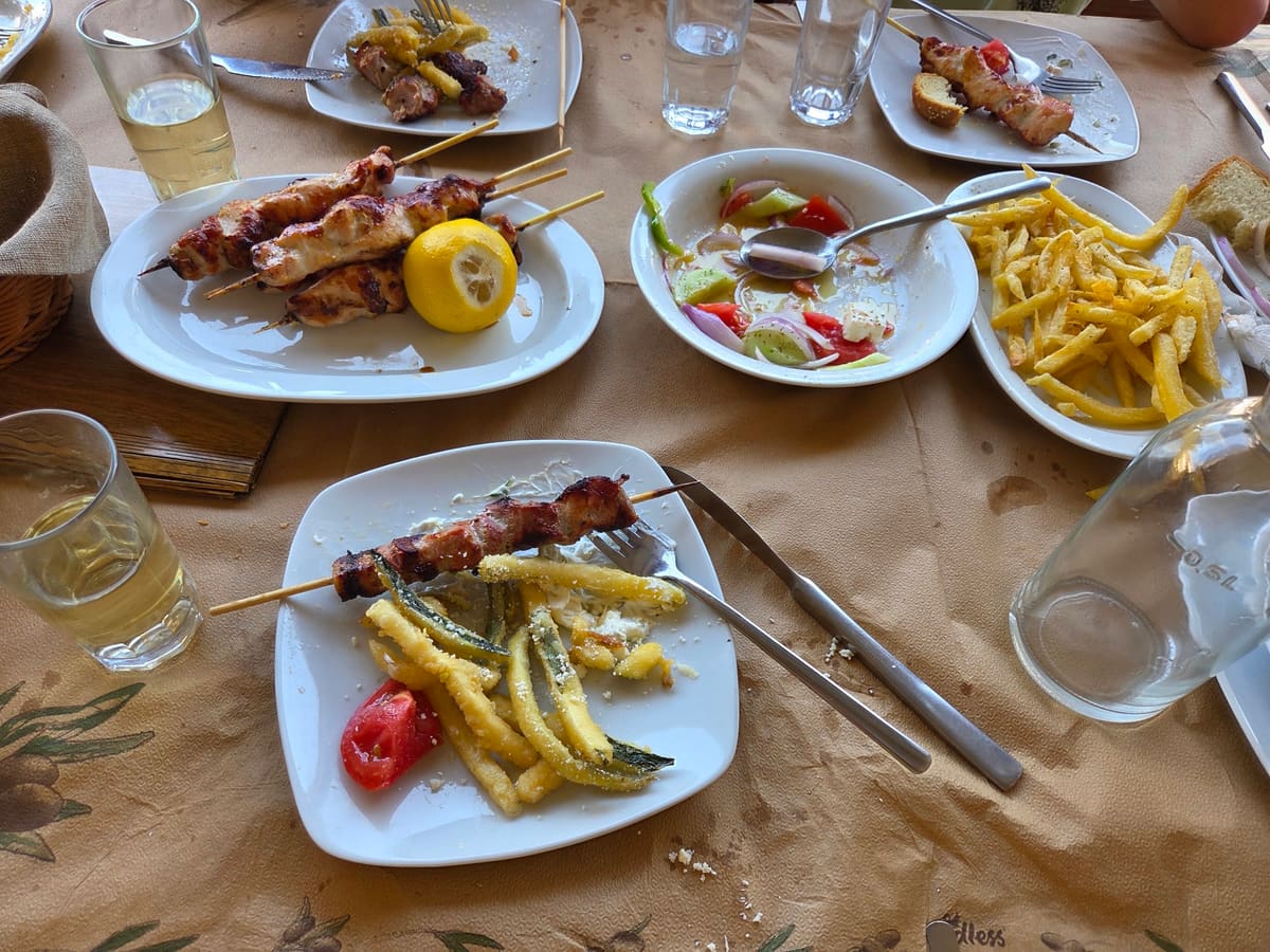 A table full of dishes: souvlaki, fried courgette, Greek salad and chips