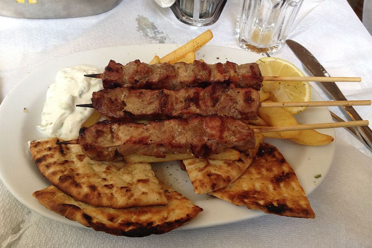 Een bord souvlakispiesjes met gegrilde pita, friet en tzatziki