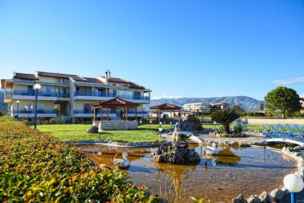 The small fish pond with stones and swan figures in the garden, with the apartment building and gazebos behind