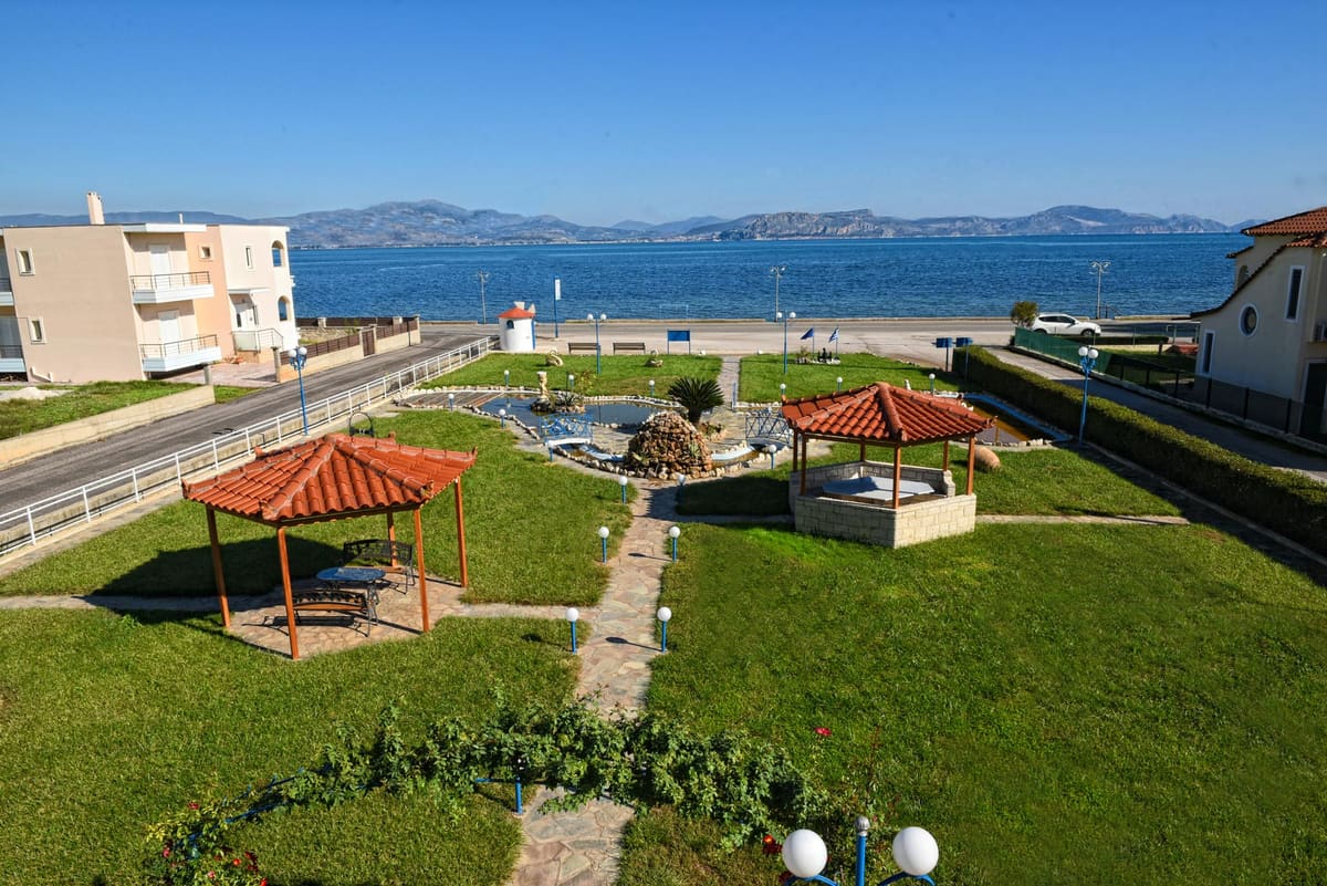 The lawn with two tiled gazebos and a stone path, the coast road and the bay with mountains beyond