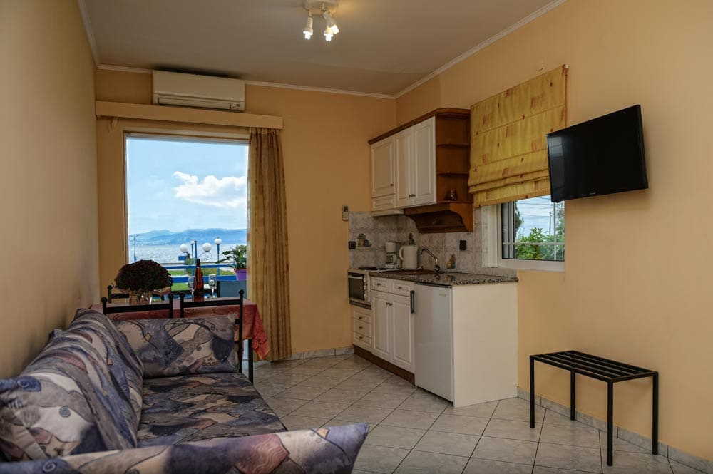 Apartment living room with a sofa, a kitchenette, a TV and a window looking out to the sea