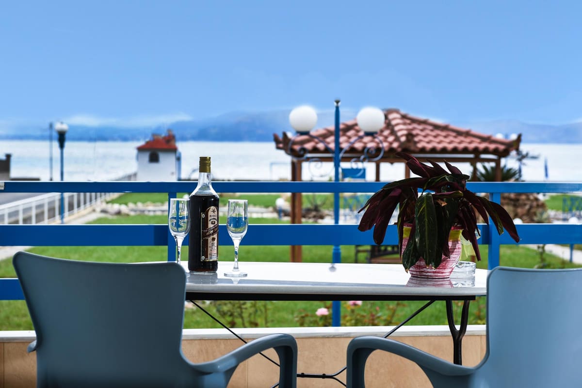 A veranda table with two chairs, a bottle and glasses, looking over the garden gazebos to the sea
