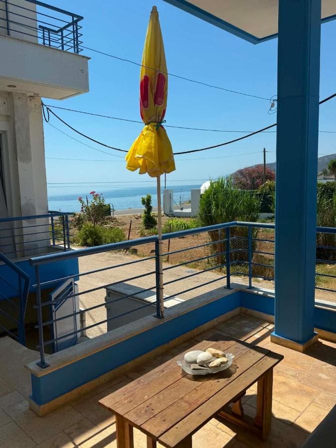 Covered balcony with blue columns, a wooden table and a parasol, looking out to the sea