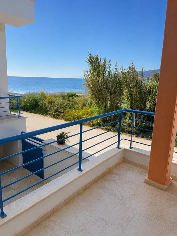 Balkon z niebieską balustradą nad ogrodem, z trzcinami i morzem w oddali