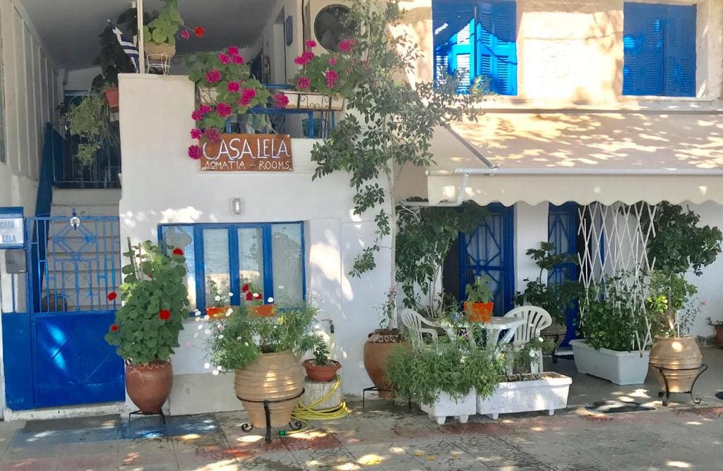 Witgekalkte ingang van Casa Lela met bloempotten en blauwe luiken