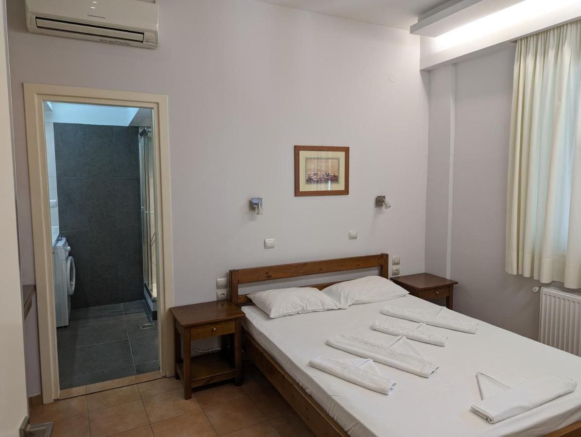 Δίκλινο δωμάτιο με ξύλινο κρεβάτι, διπλωμένες πετσέτες, κλιματιστικό και ανοιχτή την πόρτα του μπάνιου
