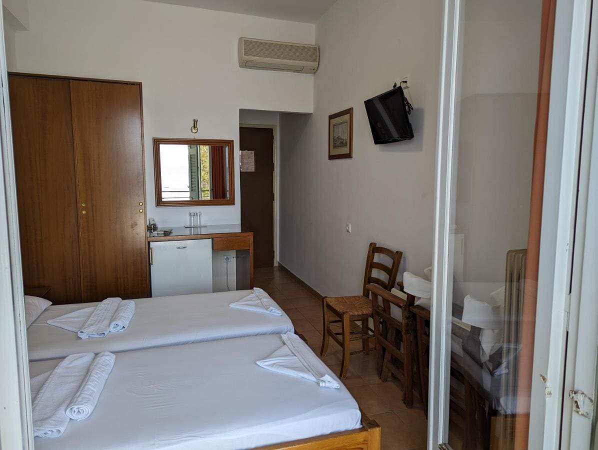 Δωμάτιο με δύο μονά κρεβάτια, ξύλινη ντουλάπα, τηλεόραση και πόρτα προς το μπαλκόνι