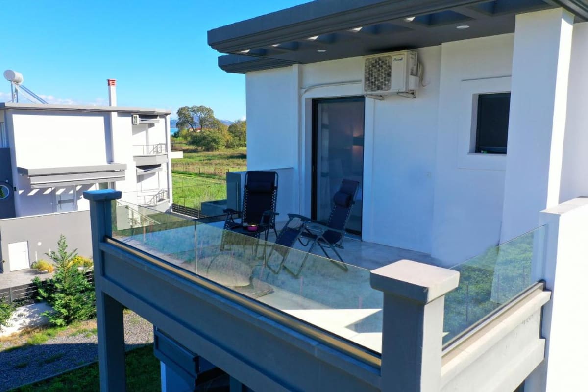 Balkon na piętrze ze szklaną balustradą i leżakami, nad ogrodem