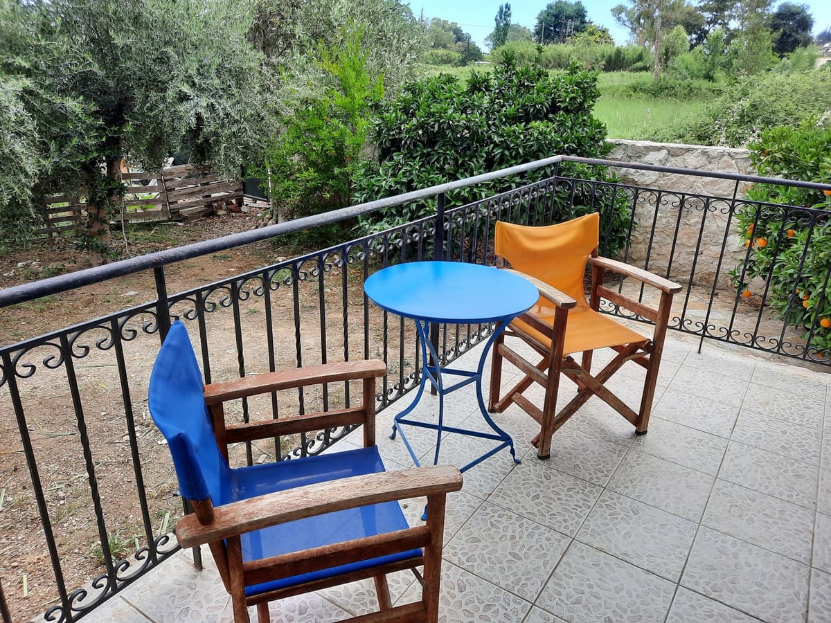Μπαλκόνι με μπλε και πορτοκαλί καρέκλες σκηνοθέτη και στρογγυλό μπλε τραπέζι, με θέα στα δέντρα του κήπου