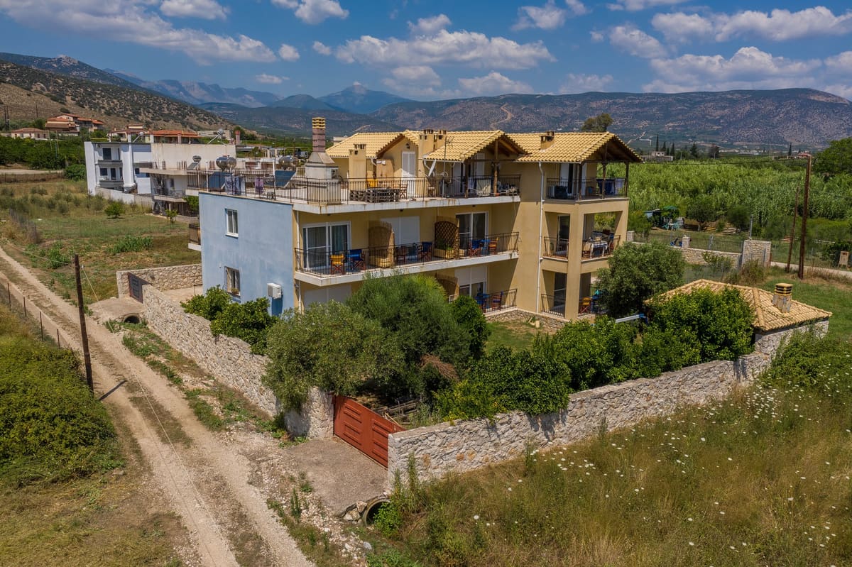 Ο Ξενώνας των Μύλων ανάμεσα στα χωράφια, με τα βουνά στο βάθος