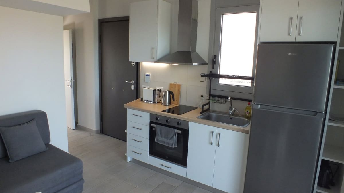 White kitchenette with oven, hob, sink and a tall fridge