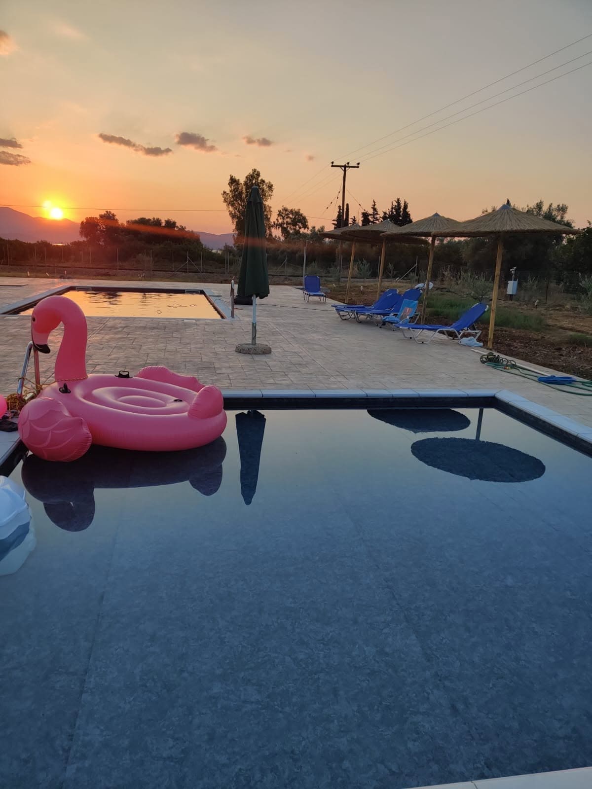 Children's pool and main pool at sunset, a pink flamingo float, reed parasols and sun loungers