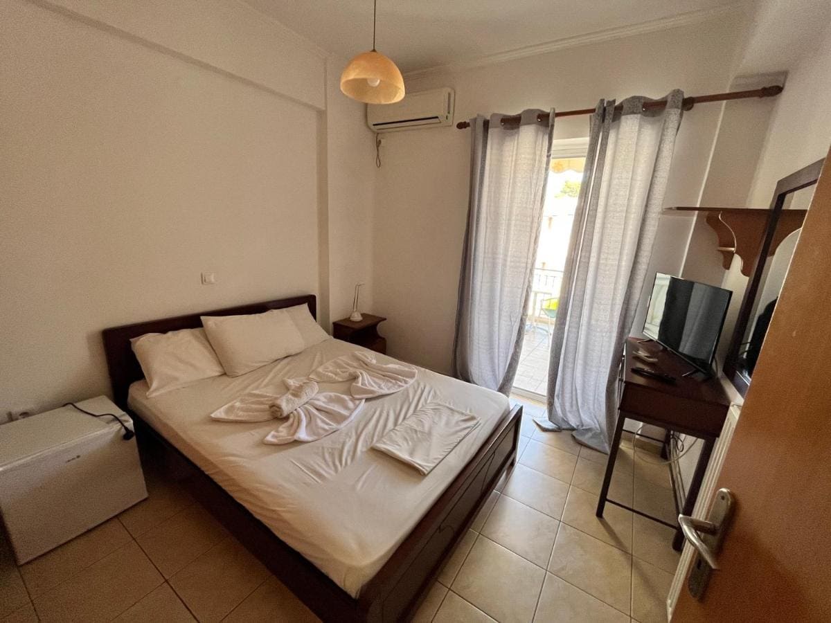 Bright bedroom with a double bed, folded towels, a desk with TV and a balcony door with white curtains
