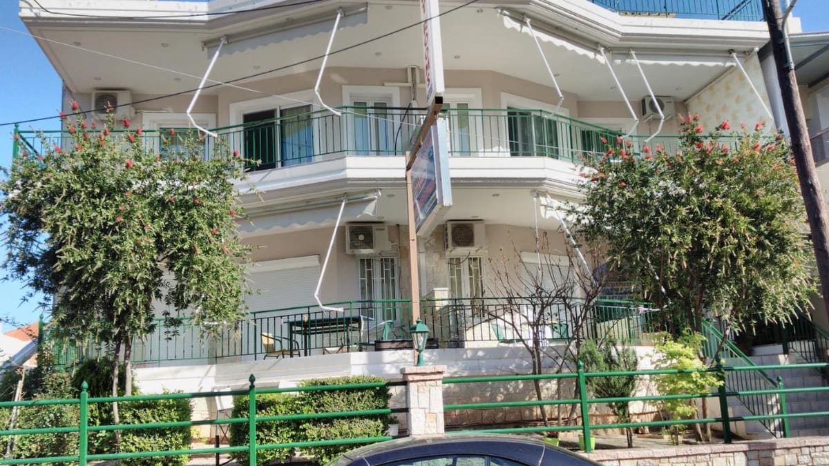 The Lerna Rooms building with green-railed balconies, awnings, flowering bottlebrush trees and a green fence