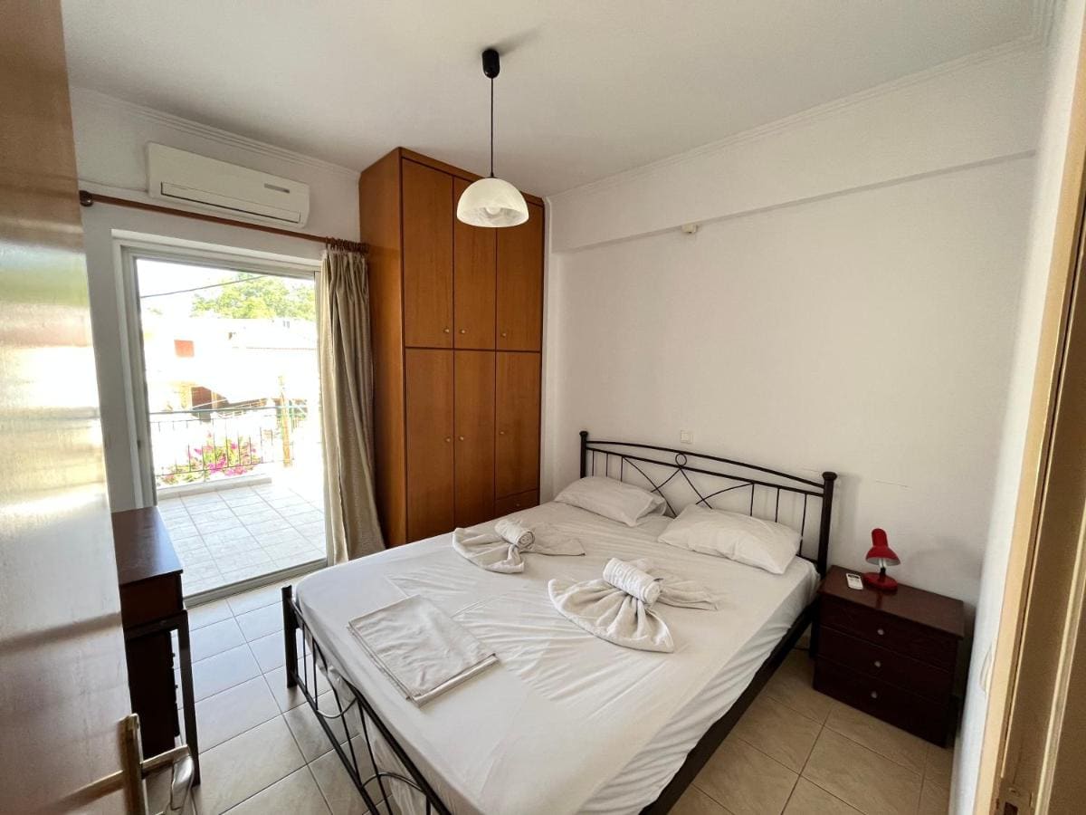 Room with a wrought-iron double bed, a wooden wardrobe, air conditioning and the balcony door open to the light