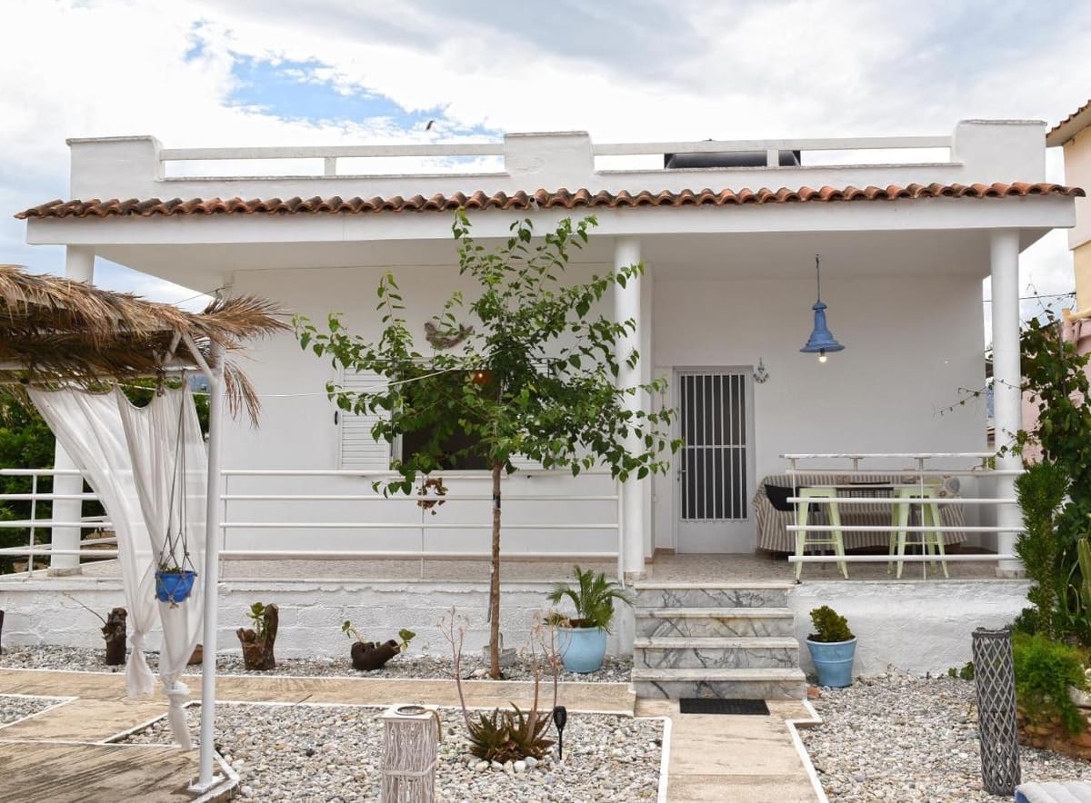 The white single-storey house with a tiled roof, a covered veranda and potted plants