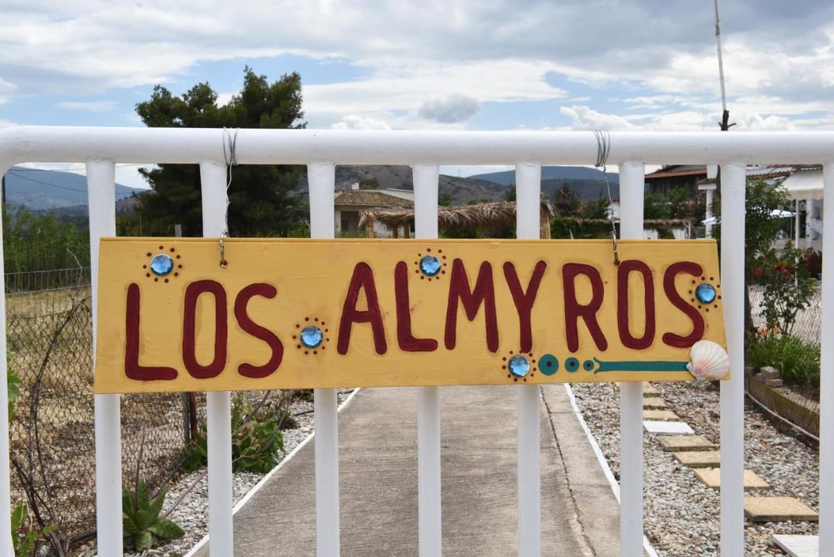 Ζωγραφισμένη στο χέρι κίτρινη πινακίδα «Los Almyros» στη λευκή αυλόπορτα