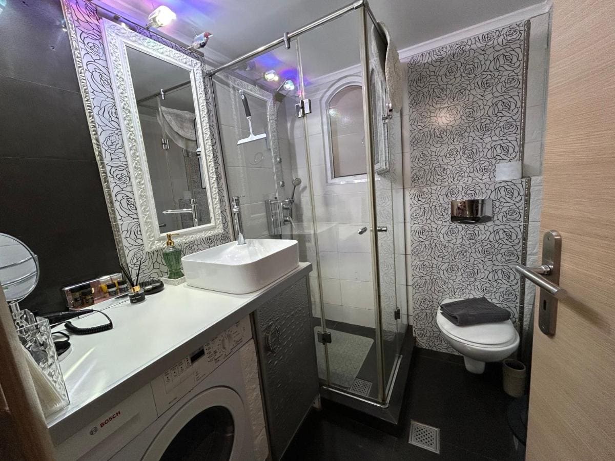 Badkamer met een glazen douchecabine, een wastafel met spiegel en een wasmachine