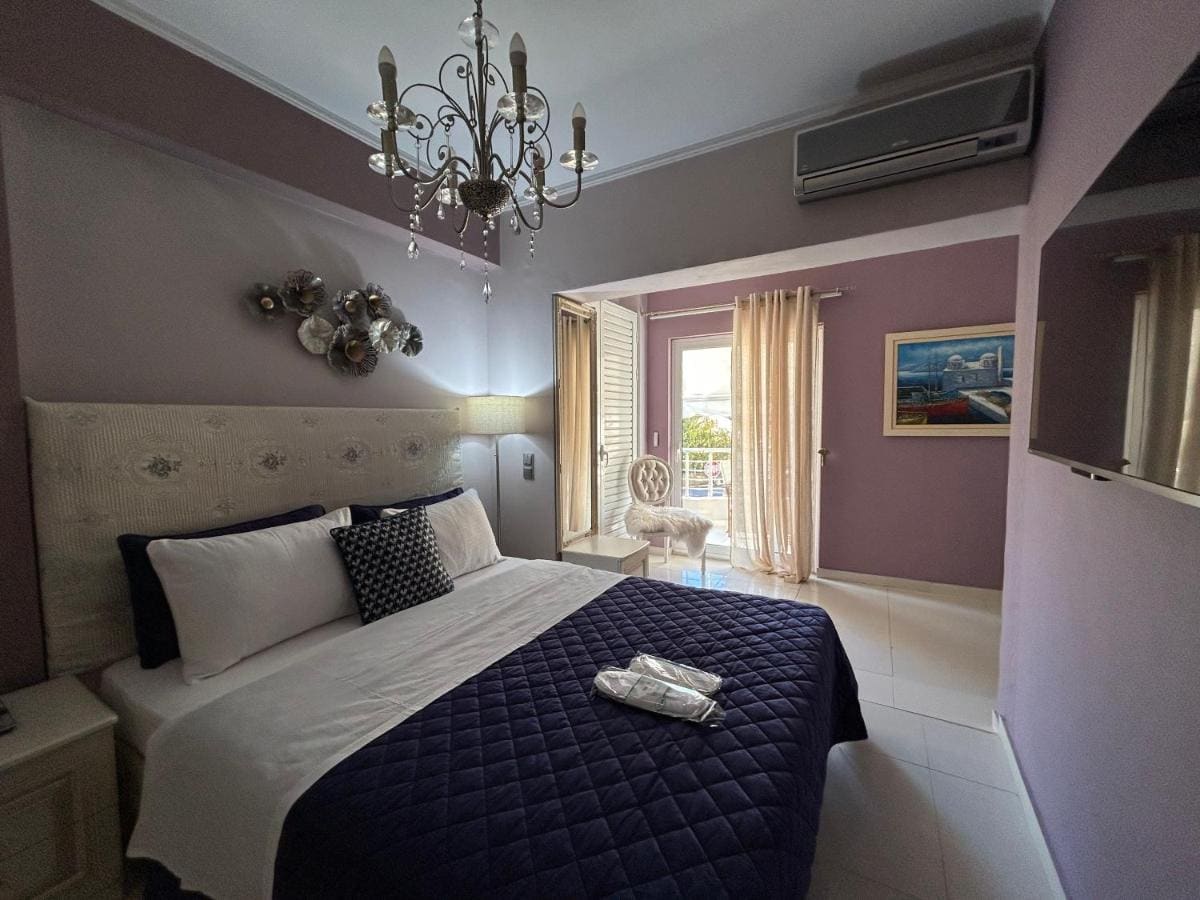 Slaapkamer met een kristallen kroonluchter, een tweepersoonsbed met donkerblauwe sprei, lila muren en een deur naar het balkon