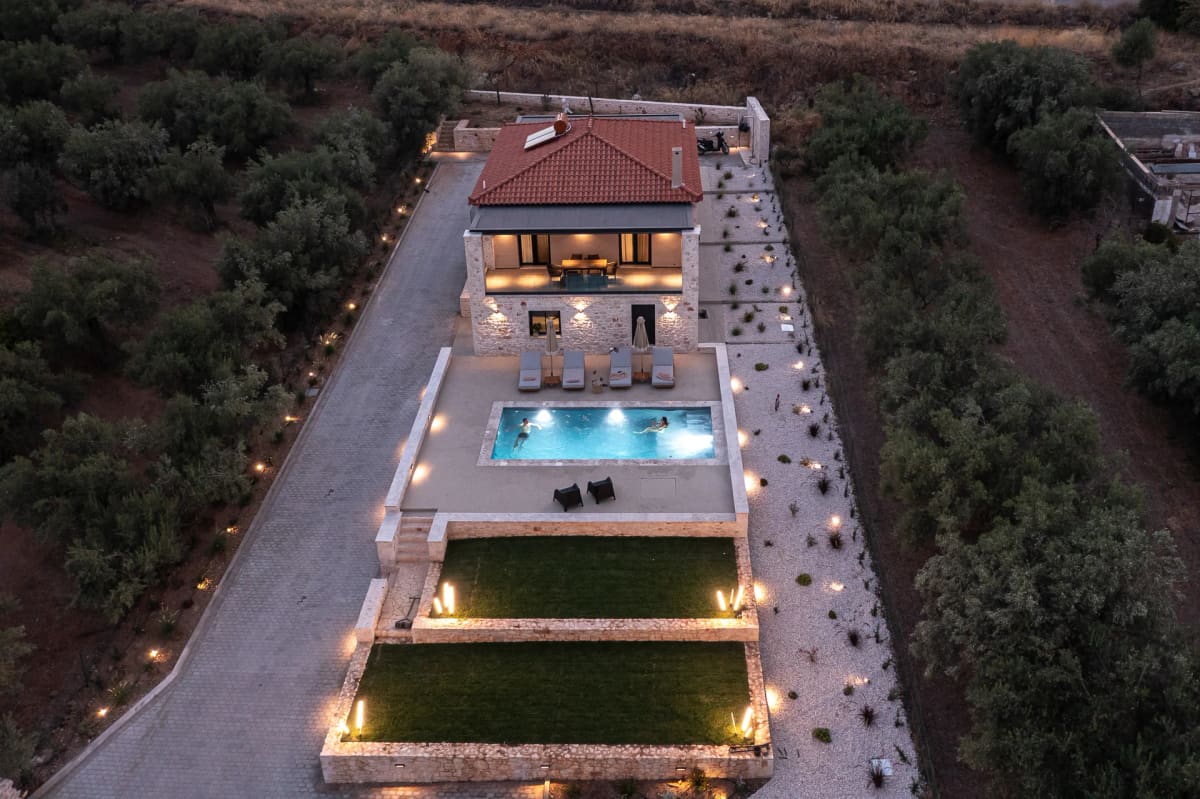The villa from the air at dusk: the lit house, pool and lawns in a long plot among olive groves