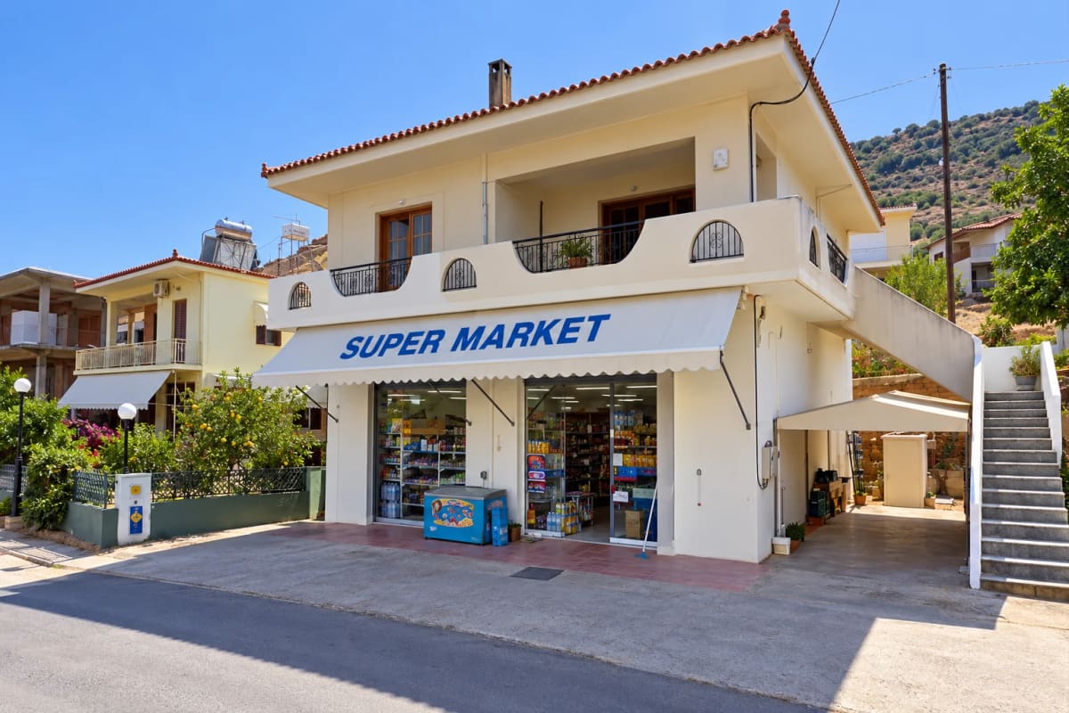 The supermarket on the ground floor of a cream-coloured house, with a white awning reading SUPER MARKET and an ice-cream freezer by the door