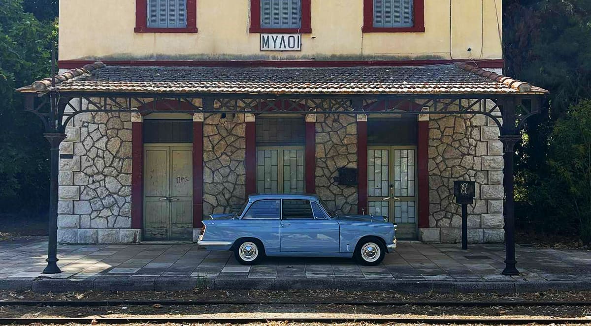 Ένα γαλάζιο Triumph Herald της δεκαετίας του 1960 μπροστά στον παλιό σταθμό των Μύλων